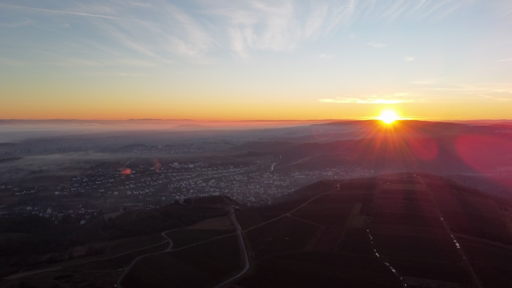 the sun is setting over a city and hills