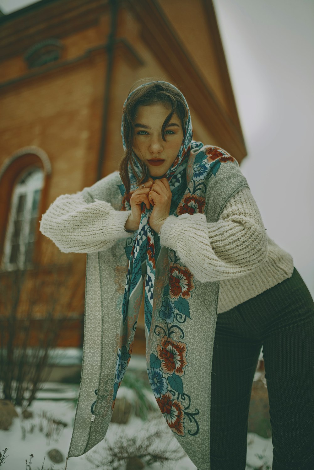 a woman standing in front of a house wearing a scarf