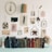 A collection of vintage books is neatly arranged on a surface, accompanied by a pastel candle and a dried flower arrangement in a cylindrical vase. Above the books, various items are creatively displayed on the wall, including framed pressed flowers, feathers, and botanical illustrations. An old hardcover book is mounted on the wall, adding to the aesthetic, which exudes a rustic and antiquarian charm.