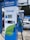 A modern electric vehicle charging station is prominently displayed with the branding 'EV Power' and a capacity of 150kW. The charger features a digital screen and contactless payment options. In the background, an electric car is partially visible under a canopy.
