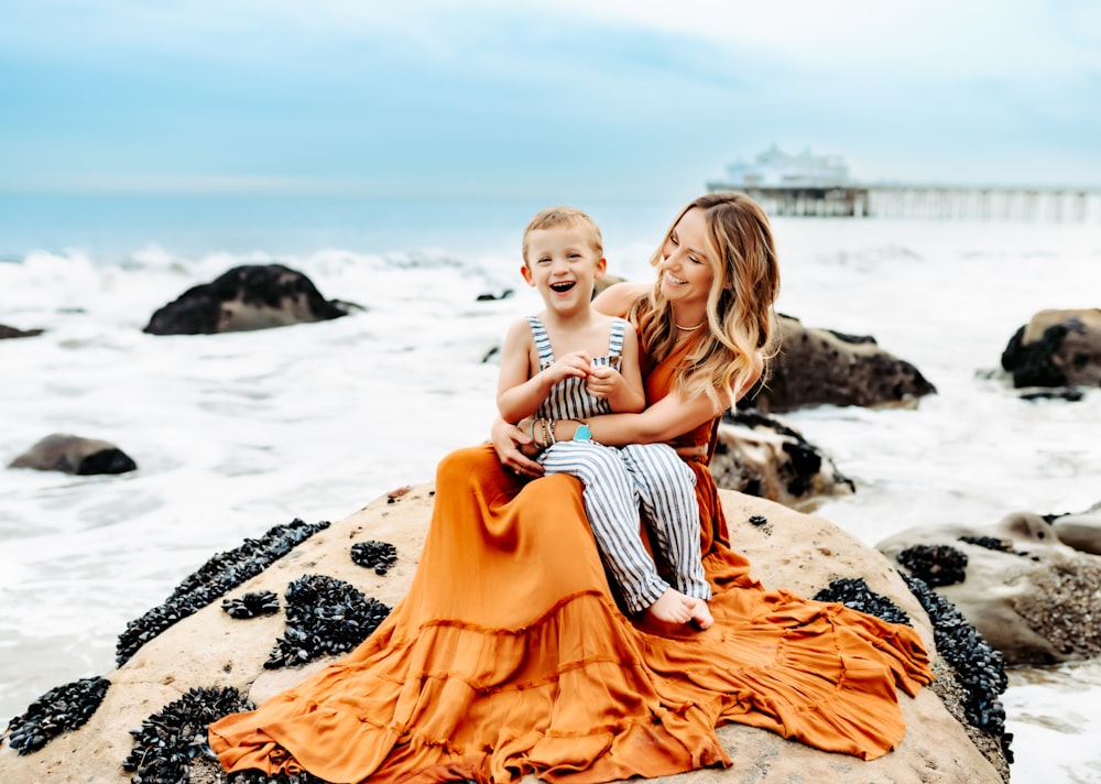 a woman and a child sitting on a rock near the ocean