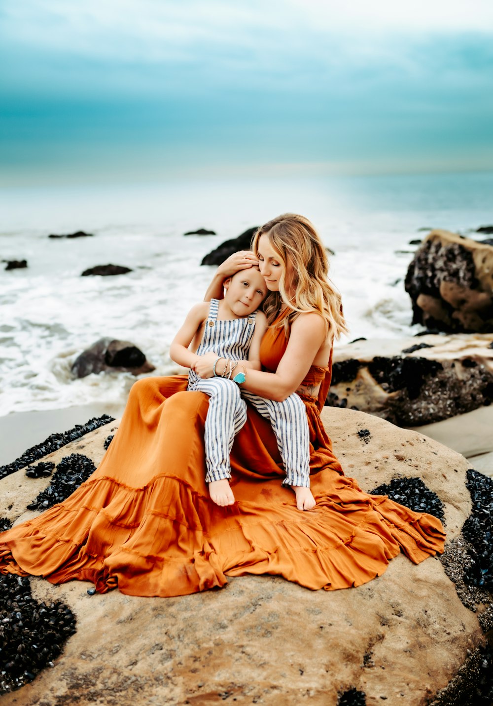 two women sitting on a rock near the ocean