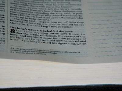 A close-up view of a book page displaying text in two columns. The heading 'The king's edict on behalf of the Jews' is bolded, and part of the biblical text from the book of Esther is visible, including prominent numbering at the start of a section.