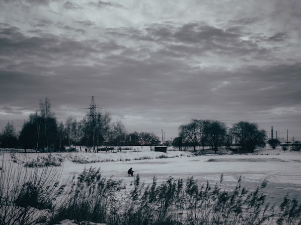 An ice fishing auger drilling through thick ice with frost-covered trees lining the horizon.