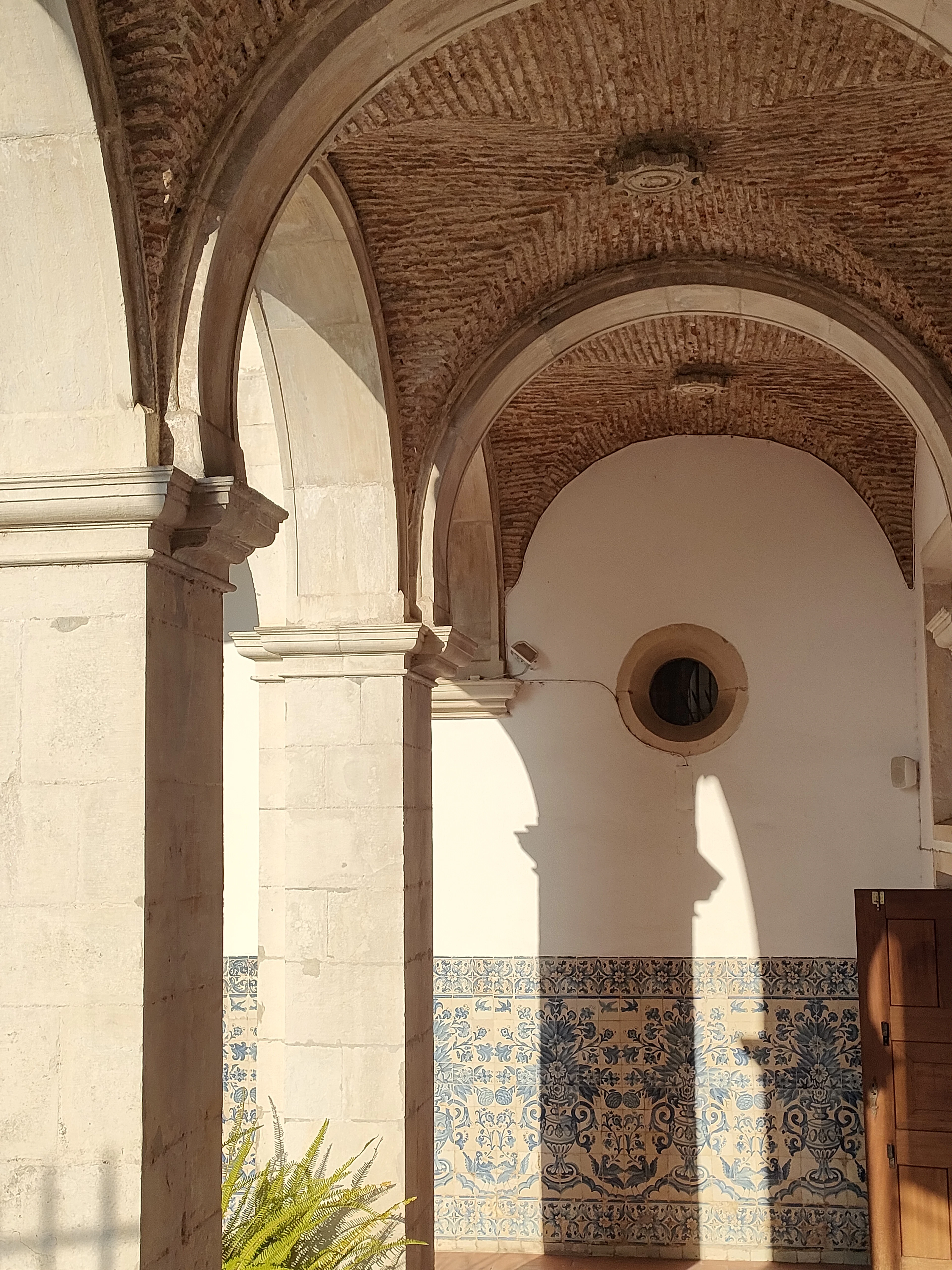A stone archway lined with blue and white tiles, in light and shadow.