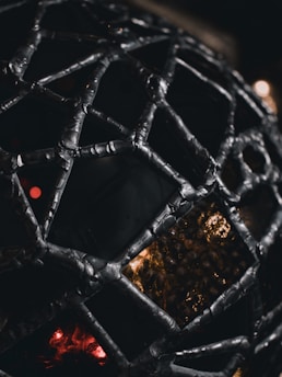 Close-up of a glowing, intricate 3D-printed lattice structure in warm amber tones against a deep black background.