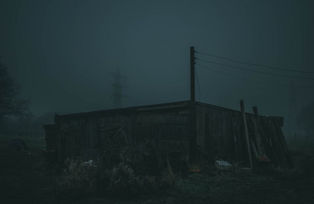 an old shack sitting in a field on a foggy night