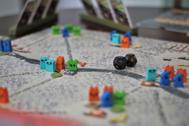 A tabletop game board with colorful wooden animal tokens and two black dice. The board is detailed with winding paths and various game cards propped up in the background.
