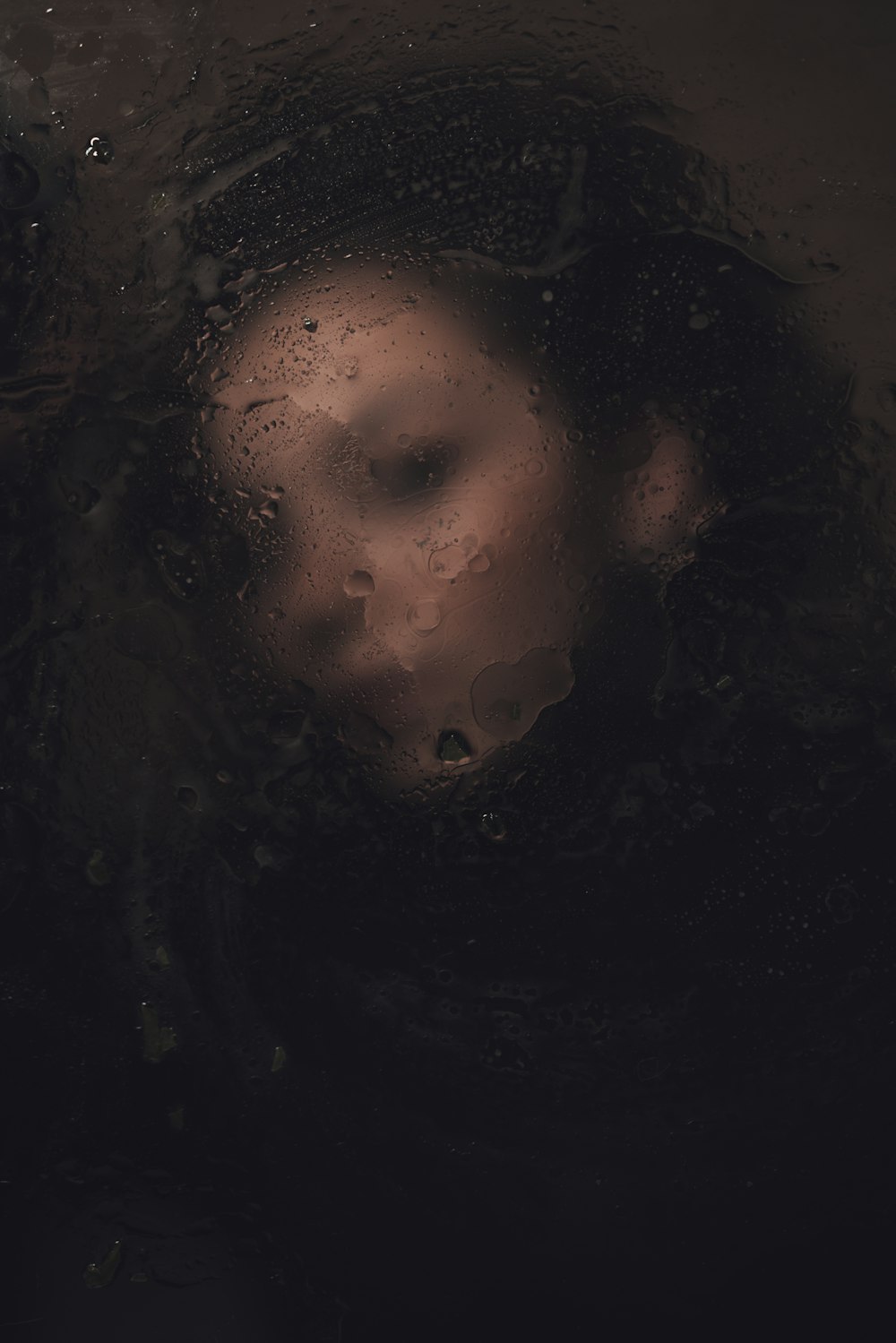 Das Gesicht einer Frau ist durch ein regenbedecktes Fenster zu sehen