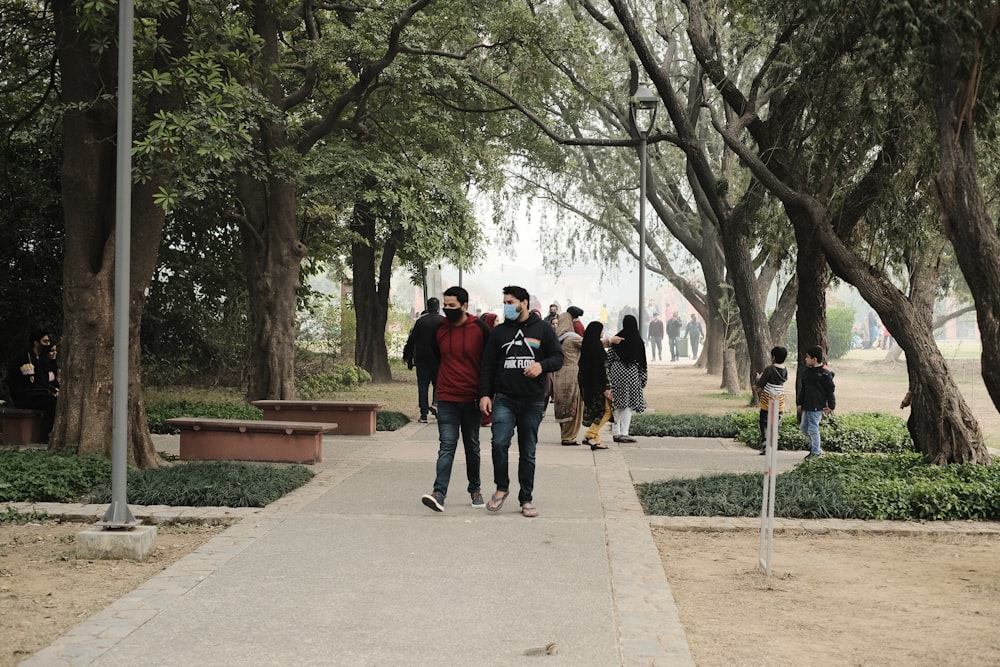 a group of people walking down a sidewalk next to trees