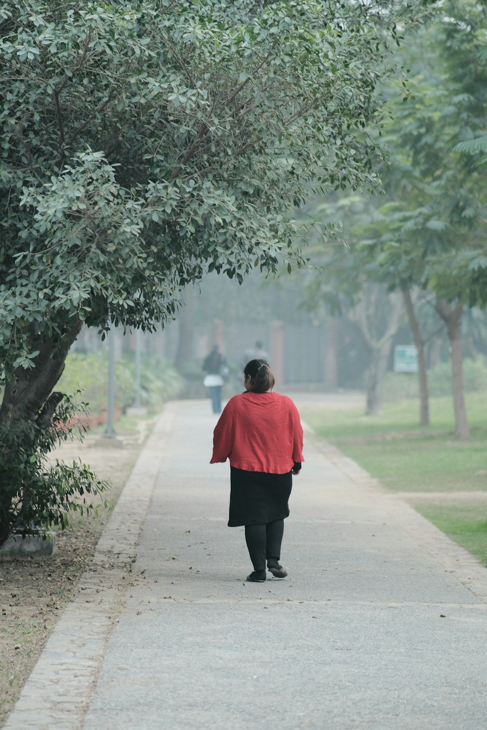 a woman walking down a sidewalk in a park
