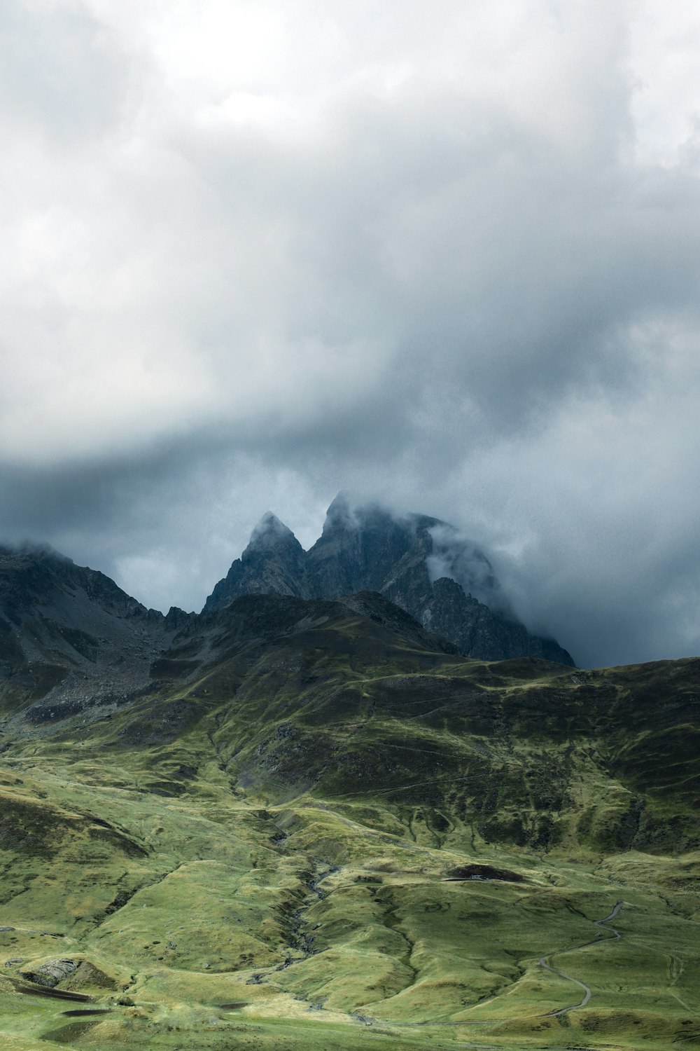 a mountain range covered in green grass under a cloudy sky