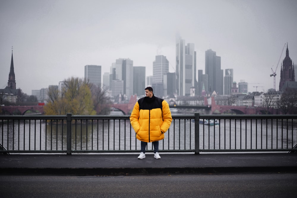 um homem em uma jaqueta amarela puffer de pé em uma ponte