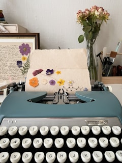 a blue typewriter sitting on top of a table next to a vase of flowers