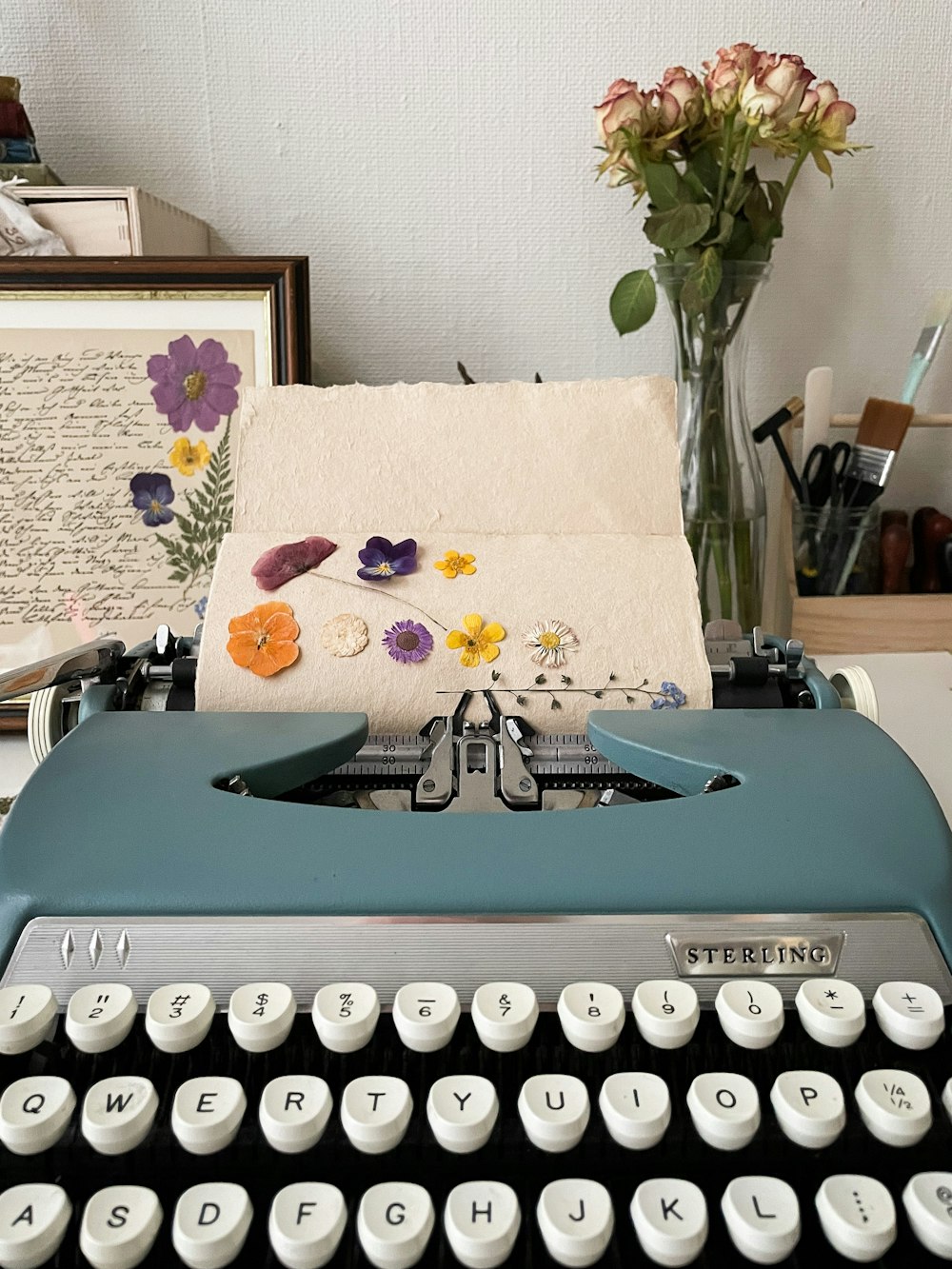 a blue typewriter sitting on top of a table next to a vase of flowers