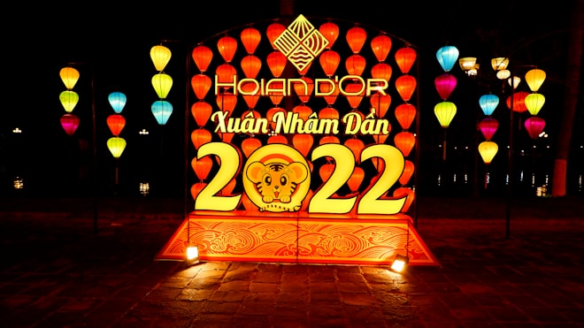 A vibrant display of colorful lanterns arranged around a central illuminated sign featuring the year 2022, with a stylized tiger face and Vietnamese text 'Hoian d'Or' and 'Xu&acirc;n Nh&acirc;m Dần'. The scene is set at night, with the lanterns emitting a warm glow, creating a festive and lively atmosphere.