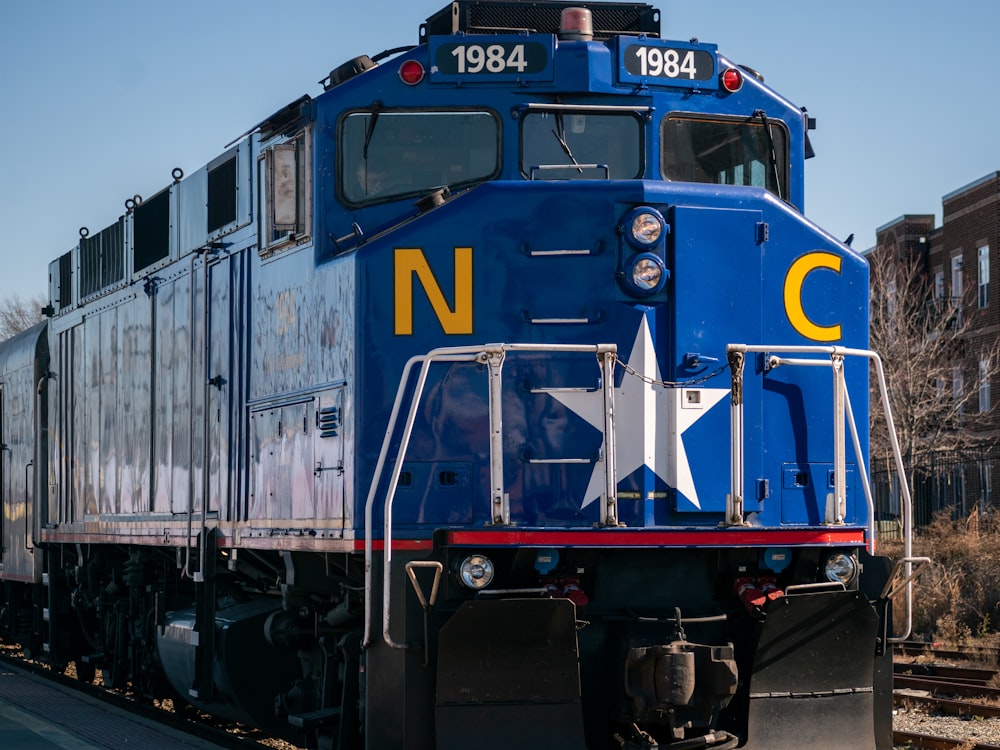 un train bleu descendant les voies ferrées à côté d’un bâtiment