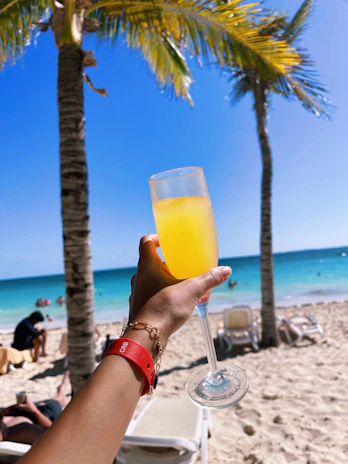 a person holding a glass of orange juice on a beach