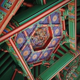 Intricate and colorful traditional ceiling decoration featuring detailed geometric patterns and ornate artwork. The design includes vibrant colors and symmetrical layouts, with a central motif that appears to depict a mythical scene.