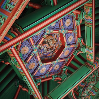Intricate and colorful traditional ceiling decoration featuring detailed geometric patterns and ornate artwork. The design includes vibrant colors and symmetrical layouts, with a central motif that appears to depict a mythical scene.
