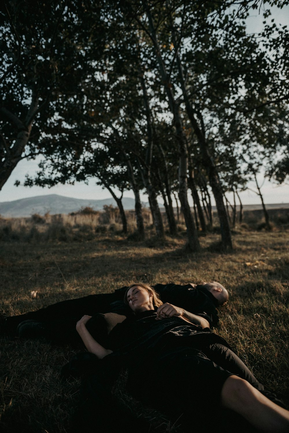 a man and a woman laying in the grass under a tree