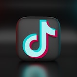 A 3D representation of a recognizable logo positioned at the center of the image. The logo is a stylized musical note with a combination of light blue and pink colors, set against a dark, glossy square background, creating a modern and sleek look.