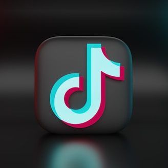 A 3D representation of a recognizable logo positioned at the center of the image. The logo is a stylized musical note with a combination of light blue and pink colors, set against a dark, glossy square background, creating a modern and sleek look.