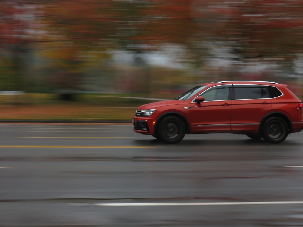 a red car driving down a street next to a forest