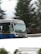 A bus is traveling at speed on a snow-covered road. The surroundings appear blurred due to motion, and evergreen trees are visible in the background. The bus is blue and silver and has a display sign at the front showing its route number.