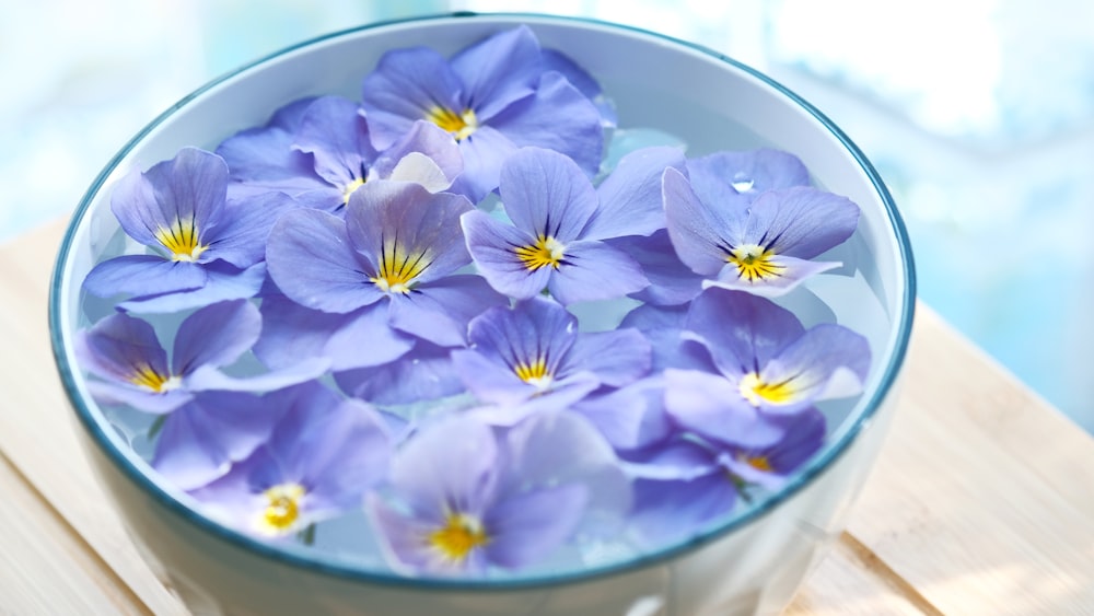 a bowl filled with purple flowers on top of a wooden table