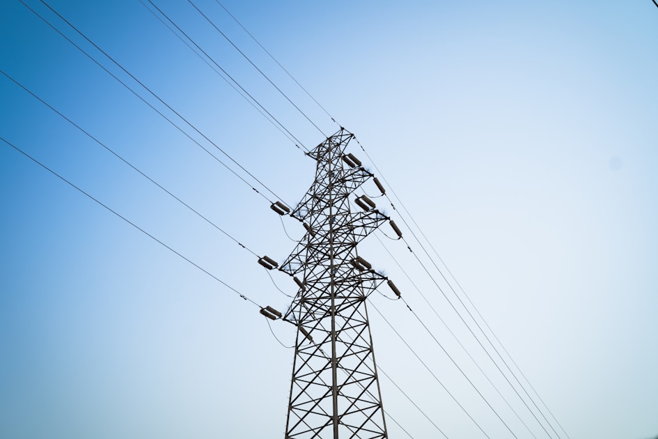 A high-voltage power transmission line silhouetted against a clear blue summer sky