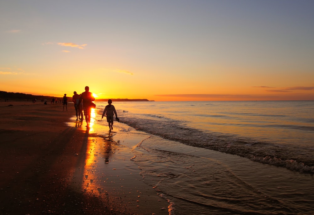 a group of people walking along a beach at sunset