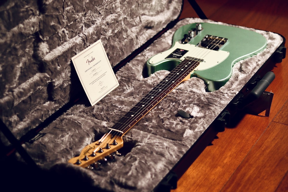 a green electric guitar in a case on a wooden floor