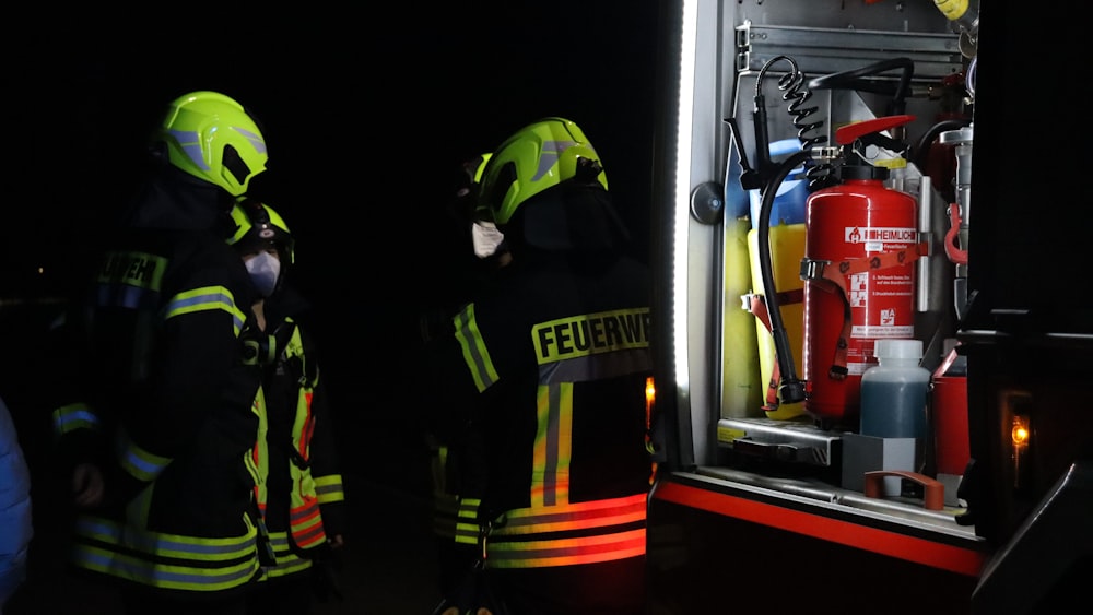 a couple of fire fighters standing next to a fire truck