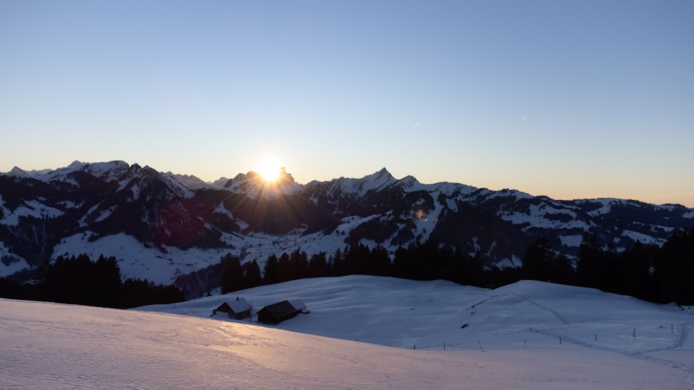 the sun is setting over a snowy mountain range