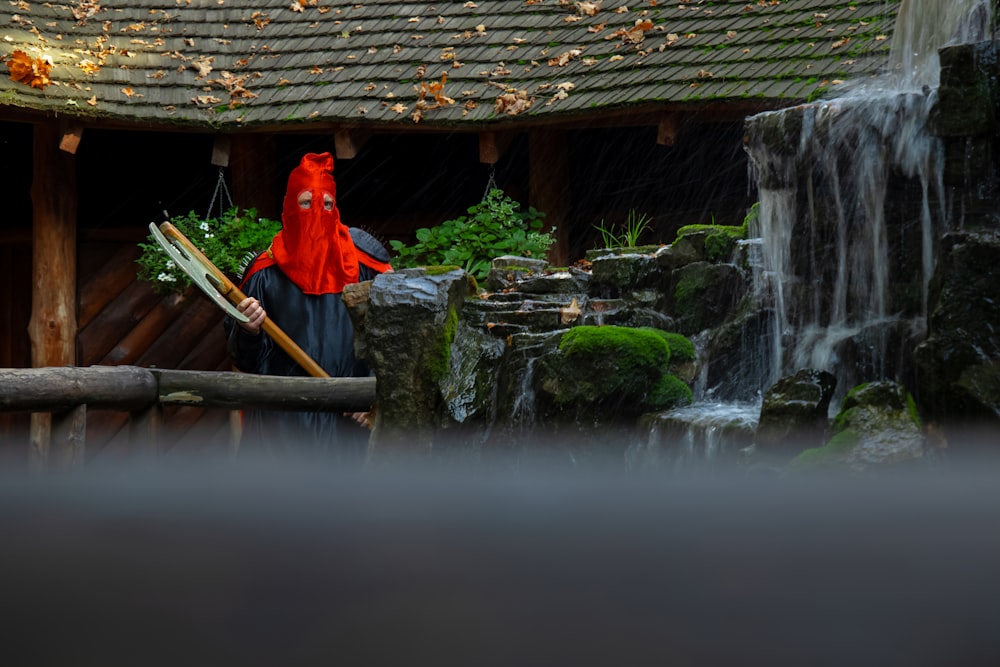 eine Person in einem roten Regenmantel steht vor einem Wasserfall