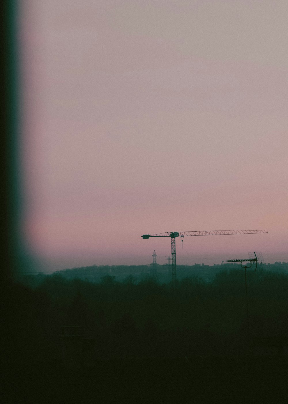 a tower crane is silhouetted against a pink sky