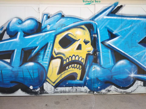 Artist spraying a vibrant red and yellow design with tiny skulls on a dark surface.