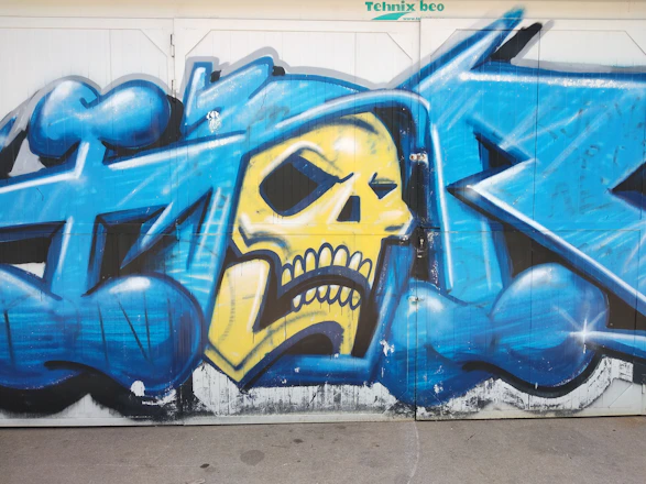 A dynamic spray paint scene featuring black, red, and yellow colors with small skulls floating subtly in the background.