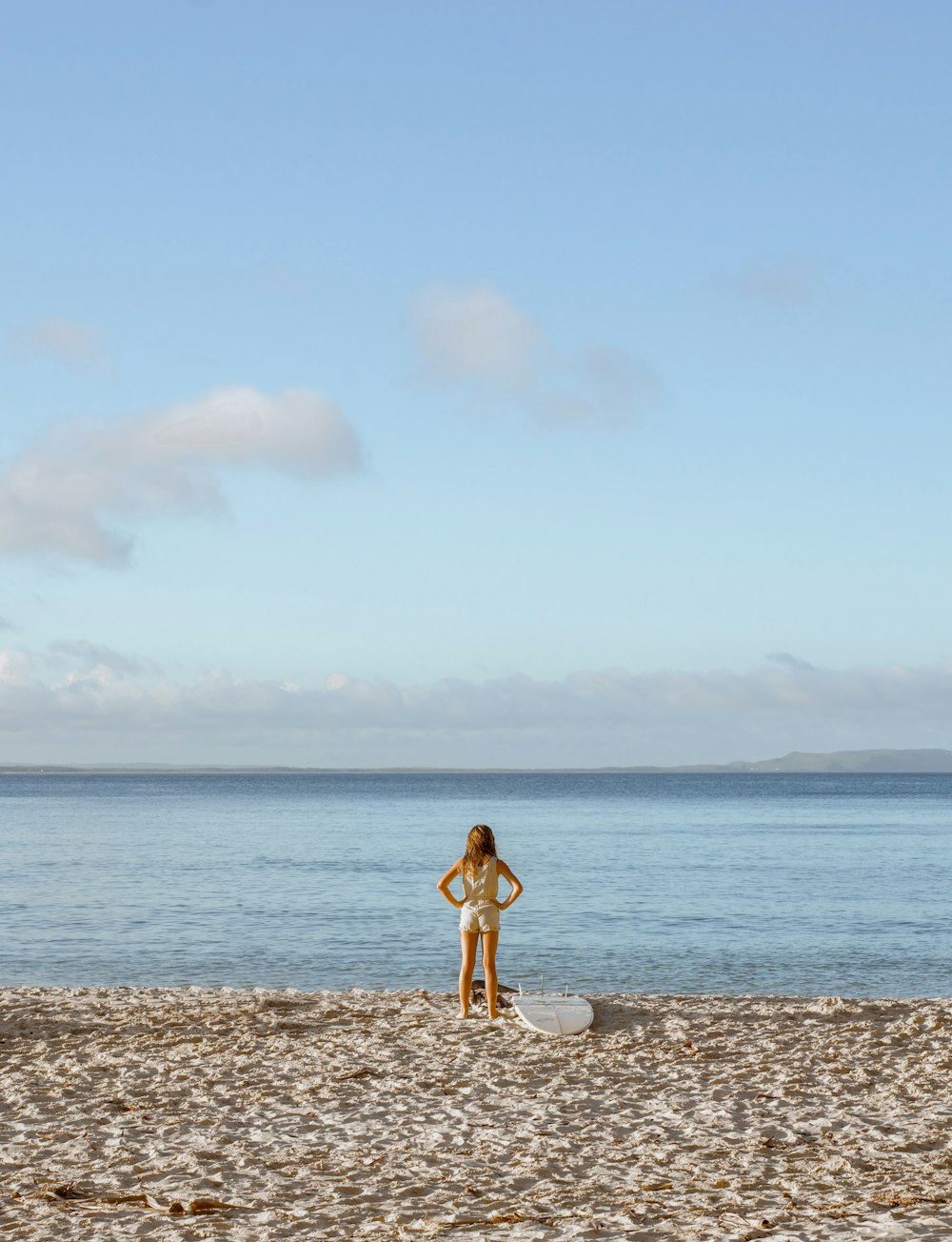 a woman standing on a beach next to a surfboard
