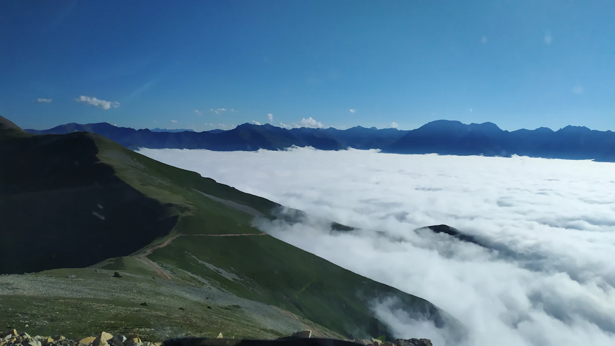 A panoramic view of Kanchenjunga peak towering above lush green valleys under a clear blue sky.