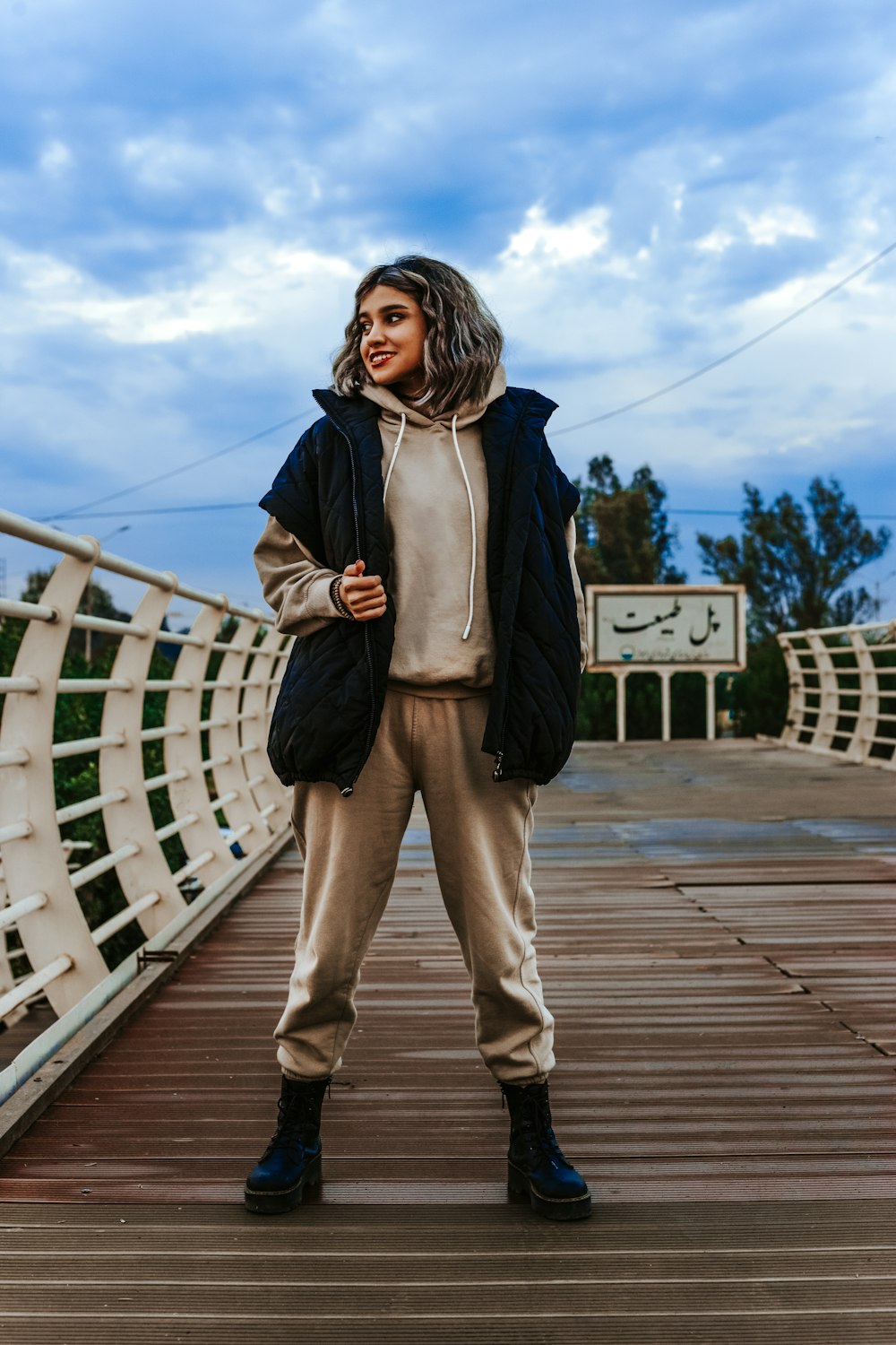 a woman standing on a bridge wearing a jacket and pants