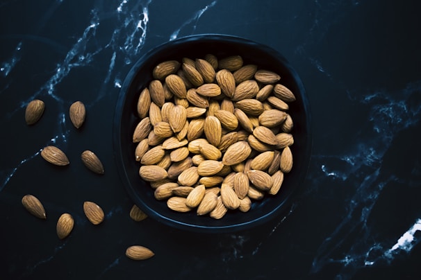 Close-up of a wooden bowl filled with glossy roasted almonds on a rustic table.