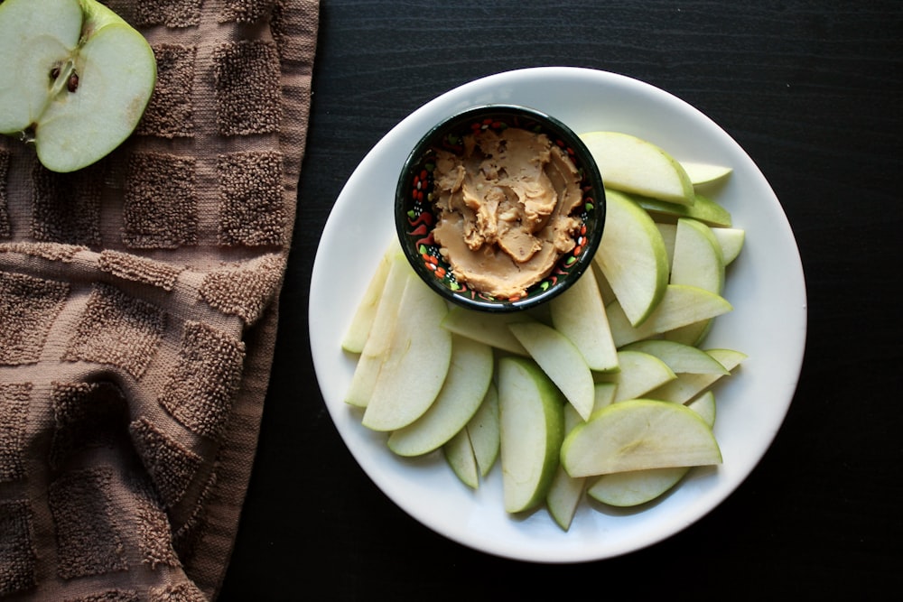 a white plate topped with sliced apples and a bowl of peanut butter