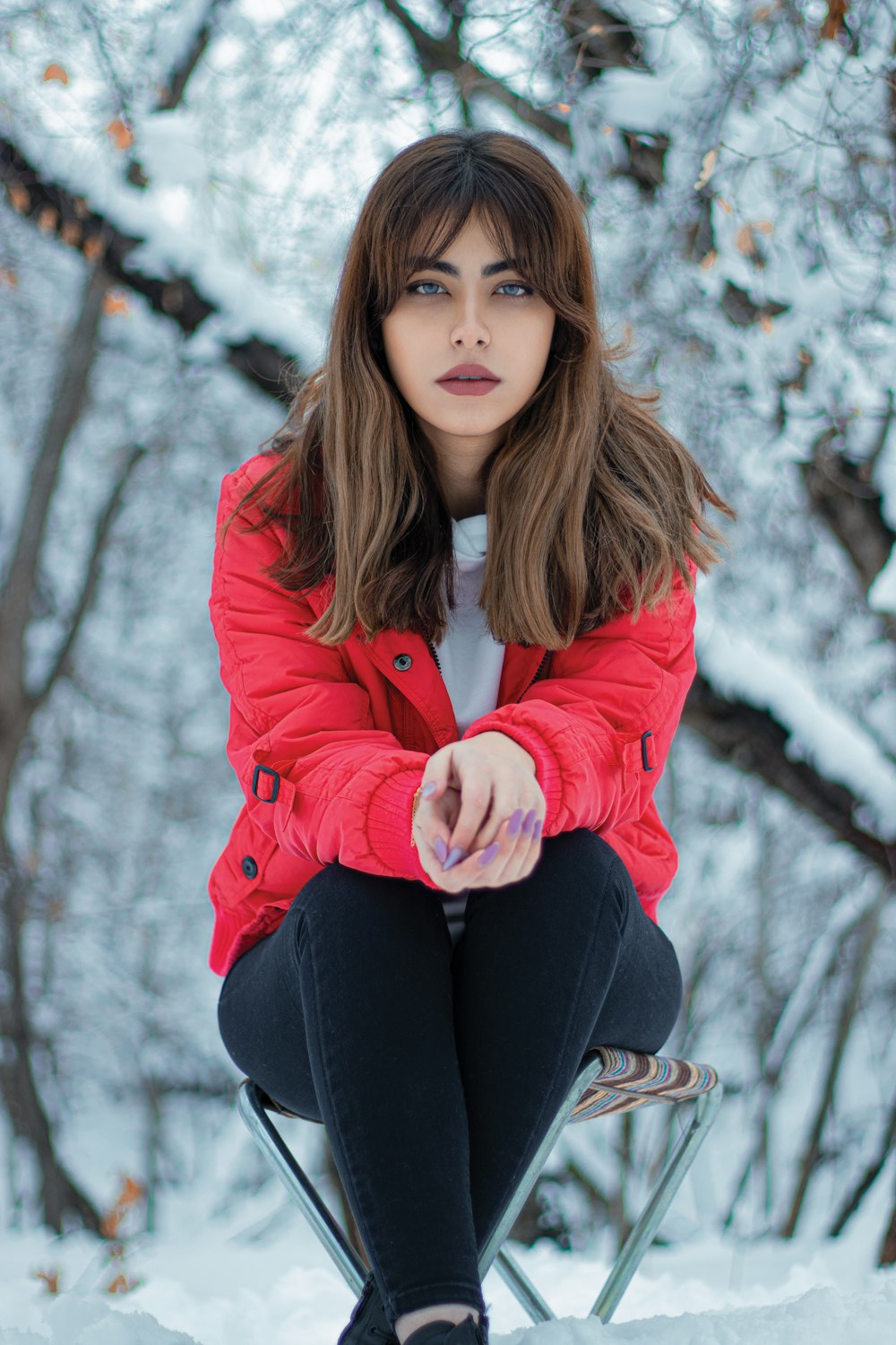 a woman in a red jacket sitting on a chair in the snow