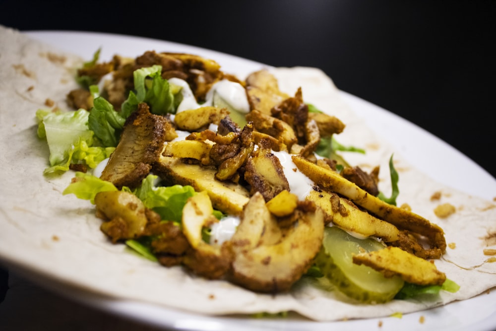 a white plate topped with a taco covered in meat and lettuce