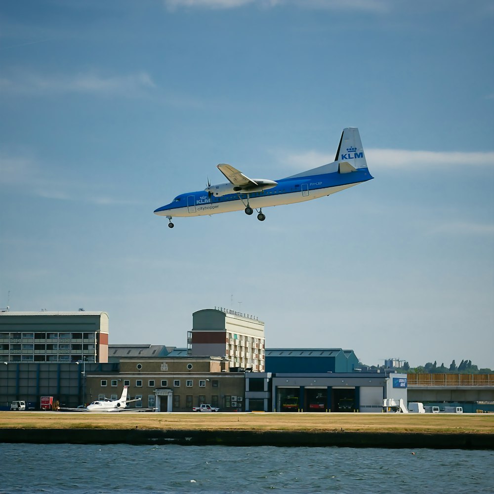 a blue and white plane flying over a body of water