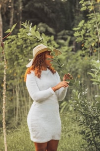 a woman in a white dress and hat holding a plant