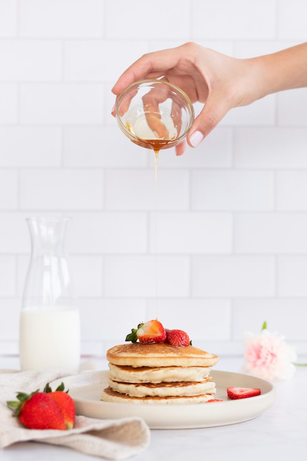 a person pouring syrup on a stack of pancakes