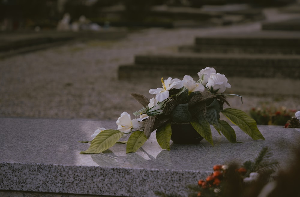 a vase with white flowers sitting on top of a cement slab